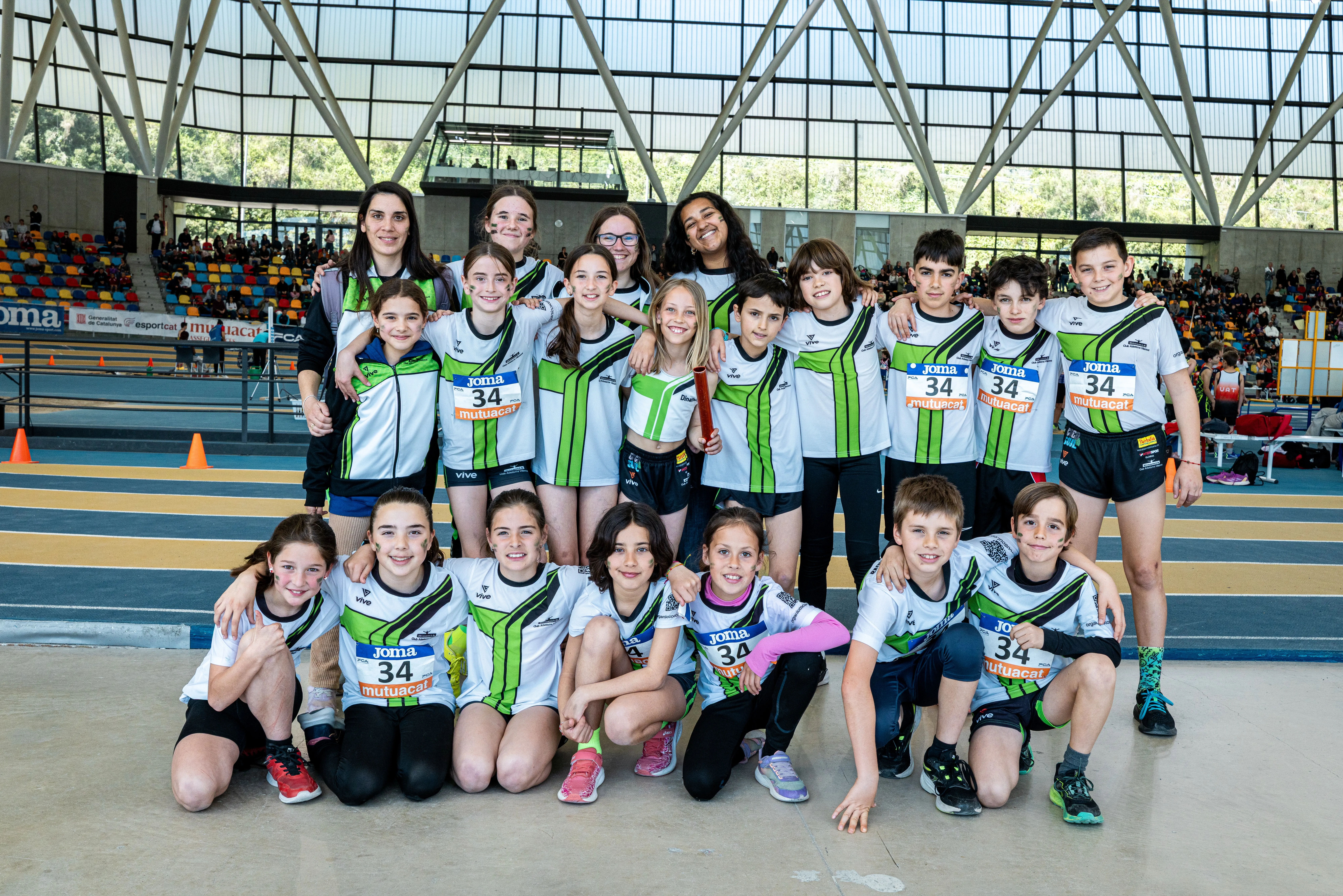 Atletes de l’escola amb la samarreta del club a la pista coberta, abraçats i somrients